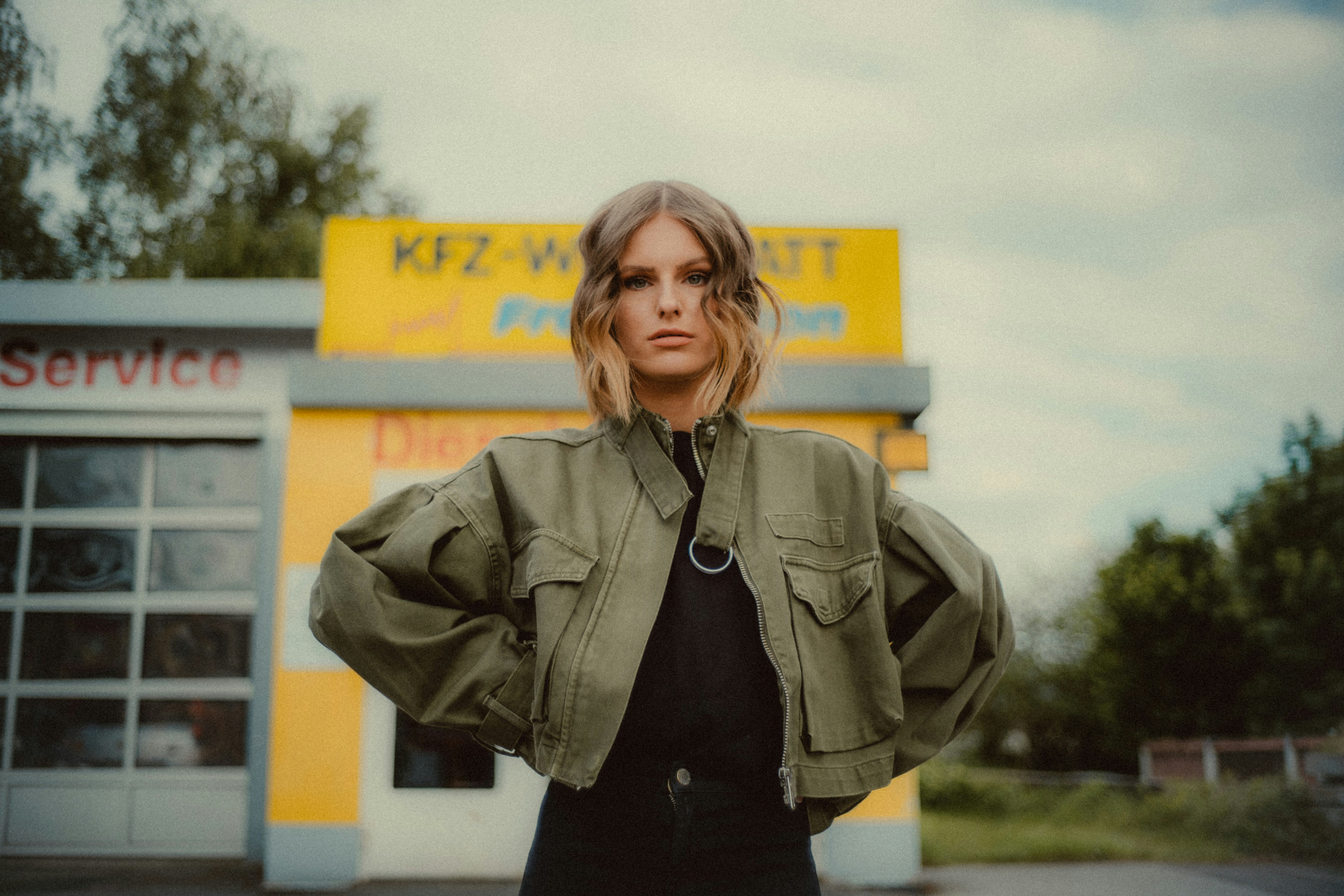 woman in brown coat standing near yellow and white building during daytime